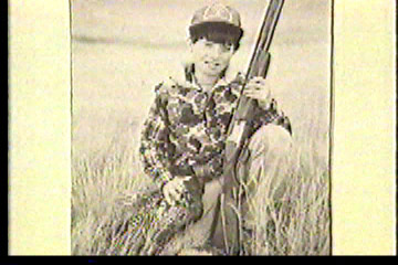 A boy, dressed in hunting attire, posing with his gun